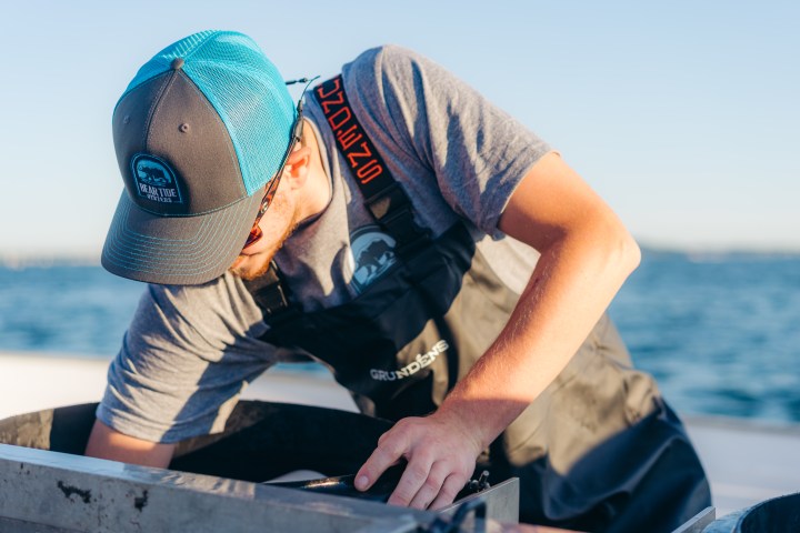 Person in cap and apron working on a boat near the sea.
