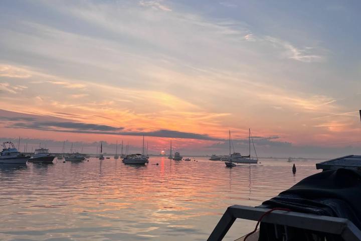 Sunset over calm bay with boats and soft clouds.