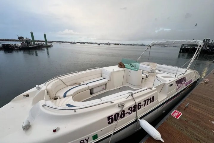 White boat docked on calm waters with overcast sky and nearby boats in the background.