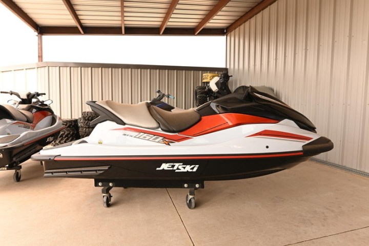 Red and white jet ski parked on concrete floor under a metal roof.