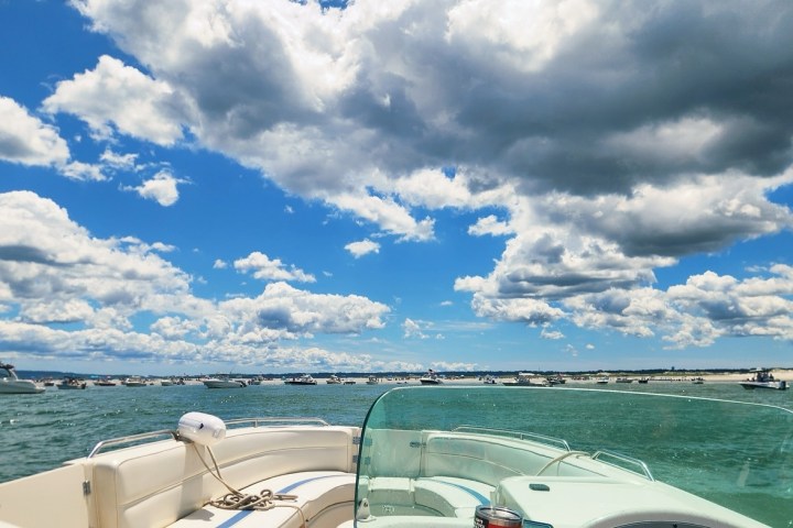 View from a boat deck towards a beach with many boats under a partly cloudy sky.